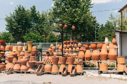 An outdoor market stall displays a large variety of terracotta pots, vases, and other ceramic items under a sunny sky.