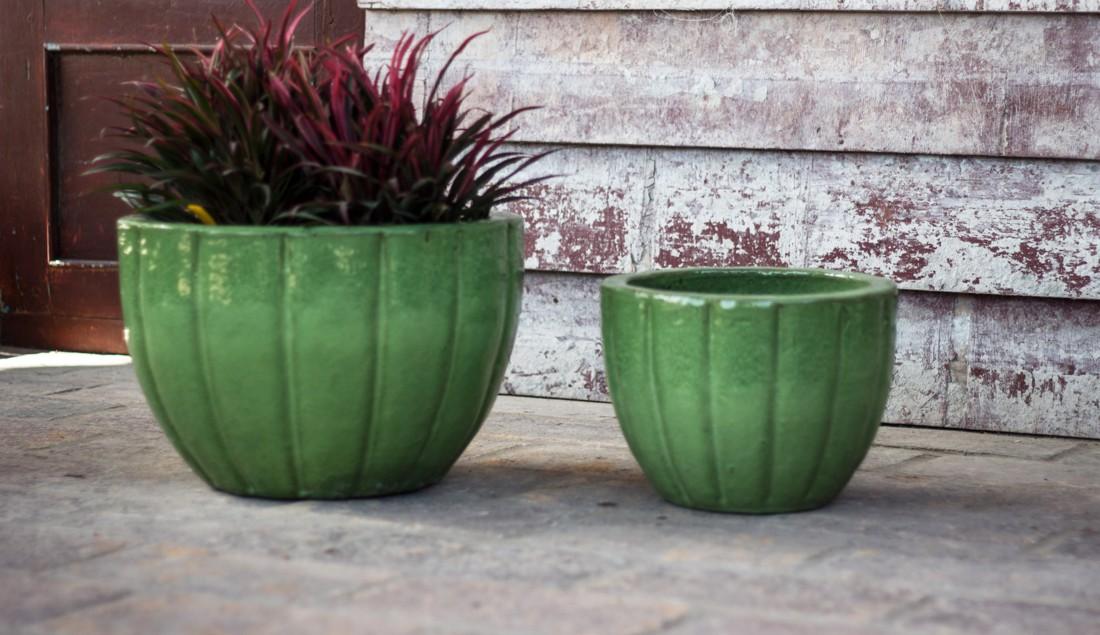 Set of two green fluted glazed ceramic planters, the larger one planted with dark red foliage, on a stone patio.