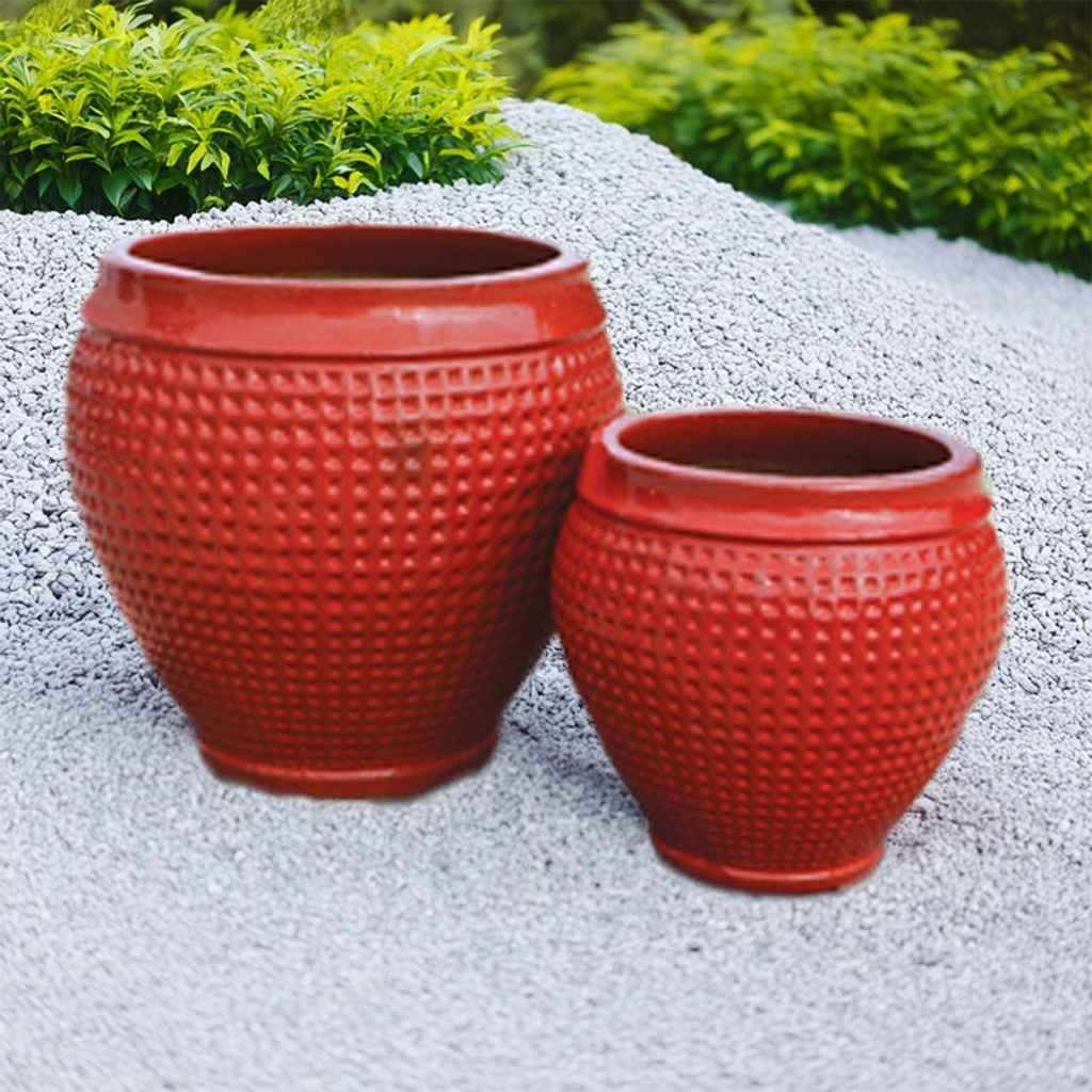 Set of two red glazed ceramic barrel planters with raised beaded texture, displayed on gravel with greenery behind.