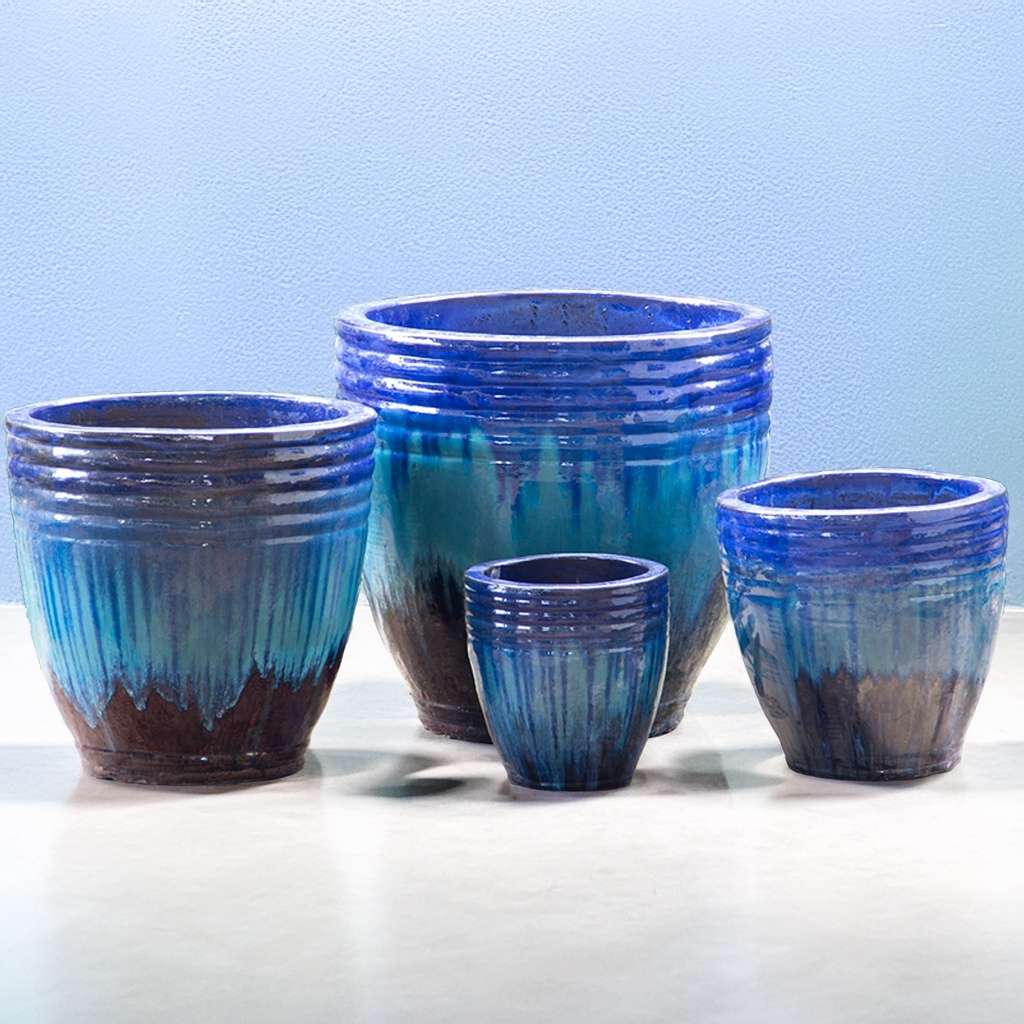 Ribbed ceramic planter in turquoise featuring a blue dripping glaze, brown base, and horizontal banding
