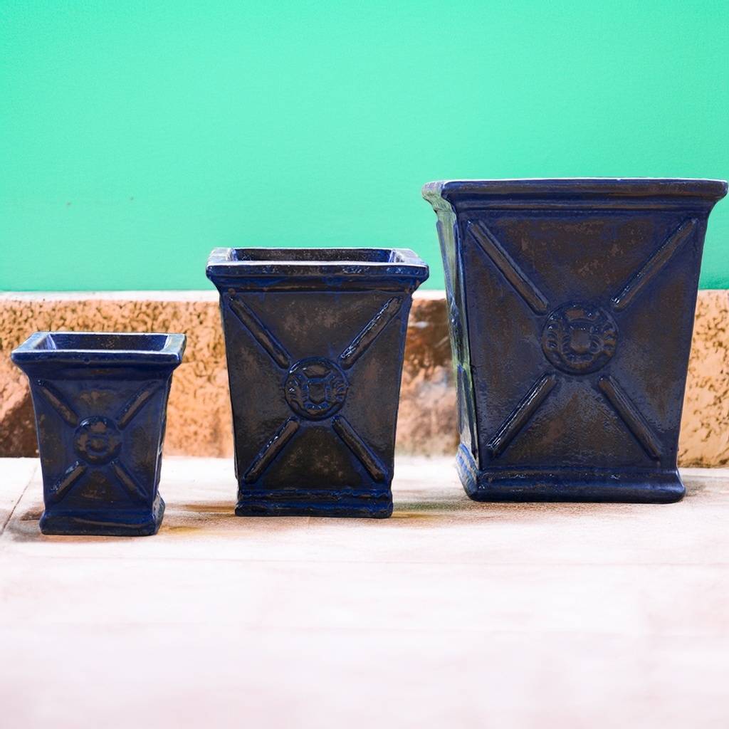 Square ceramic planter in rustic blue with brown accents, featuring a flared rim and embossed regal motif