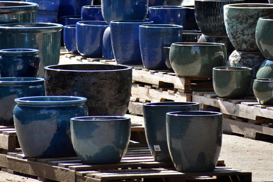 A large collection of ceramic garden pots in various shades of blue and green, displayed on wooden pallets outdoors.