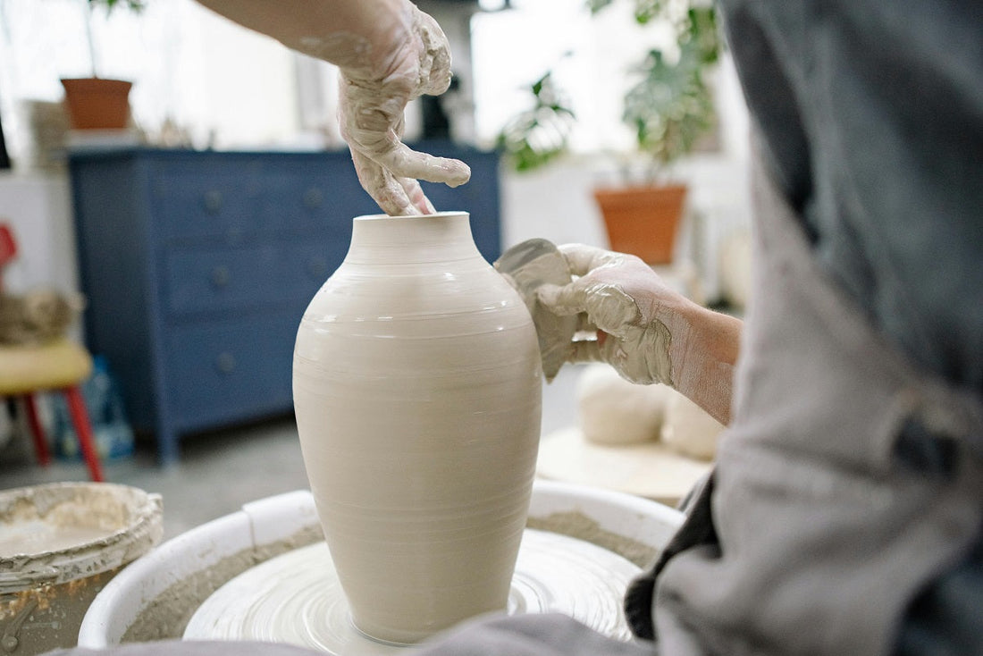 An artisan’s hands, covered in clay, shaping a tall, elegant vase on a potter's wheel.