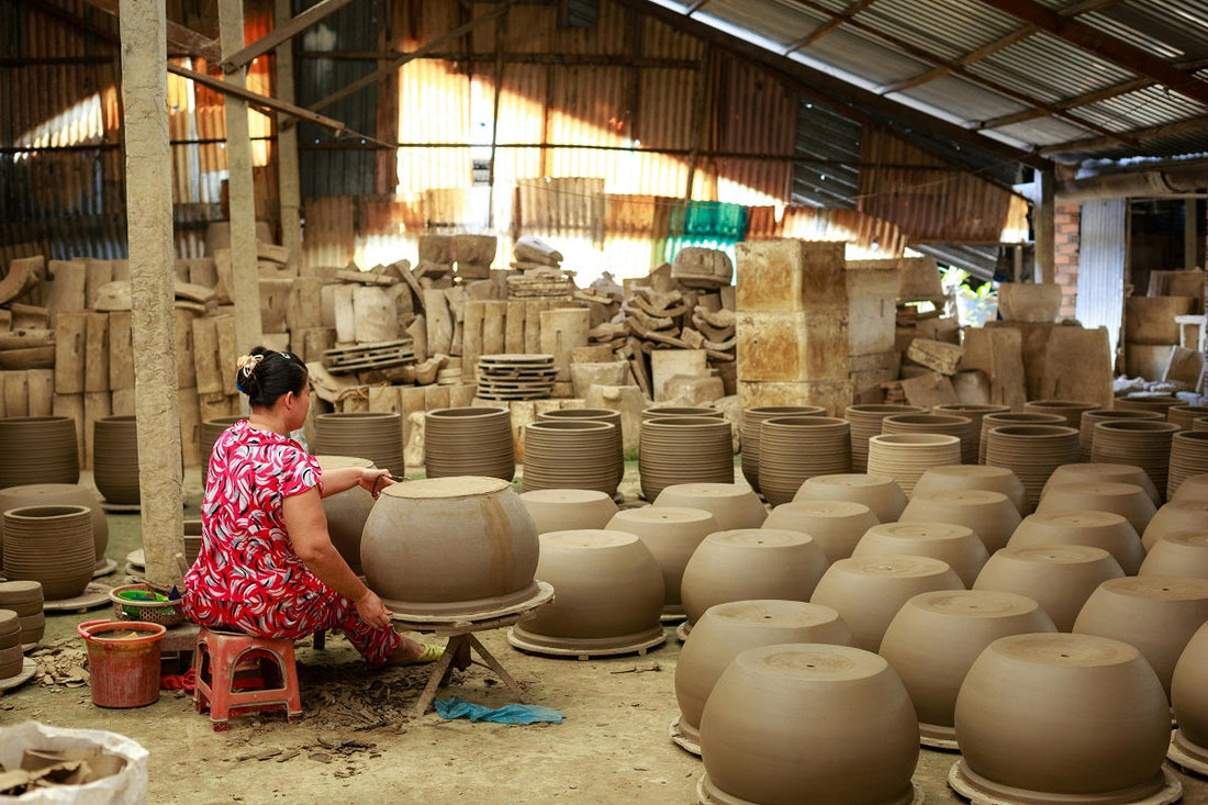 A woman works on a clay pot amidst hundreds of unglazed pottery pieces.