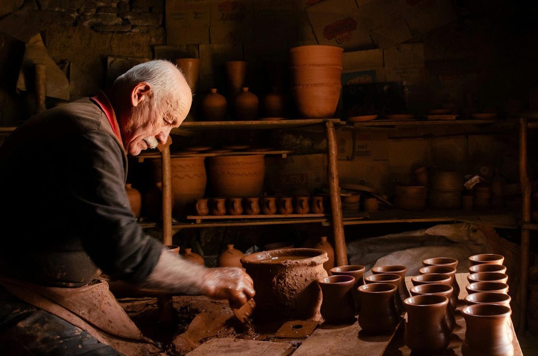 An elderly potter works in his dimly lit studio, shaping clay on a wheel.