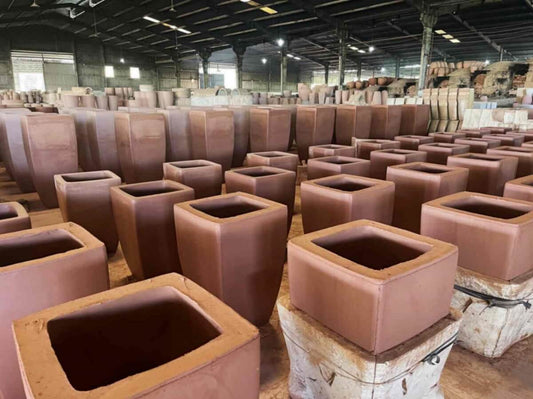 A pottery factory is filled with rows of planters in various sizes and shapes, neatly stacked.