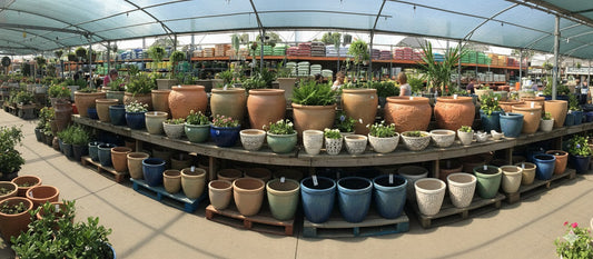 Ceramic plant pots in various sizes and colors displayed in a vibrant garden center under a shaded canopy