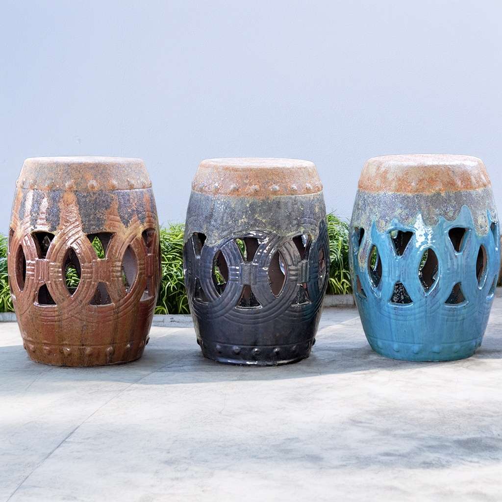 Ceramic garden stools in reddish-brown, dark blue or grey, and light blue hues, each featuring decorative cut-out shapes for a stylish and functional design