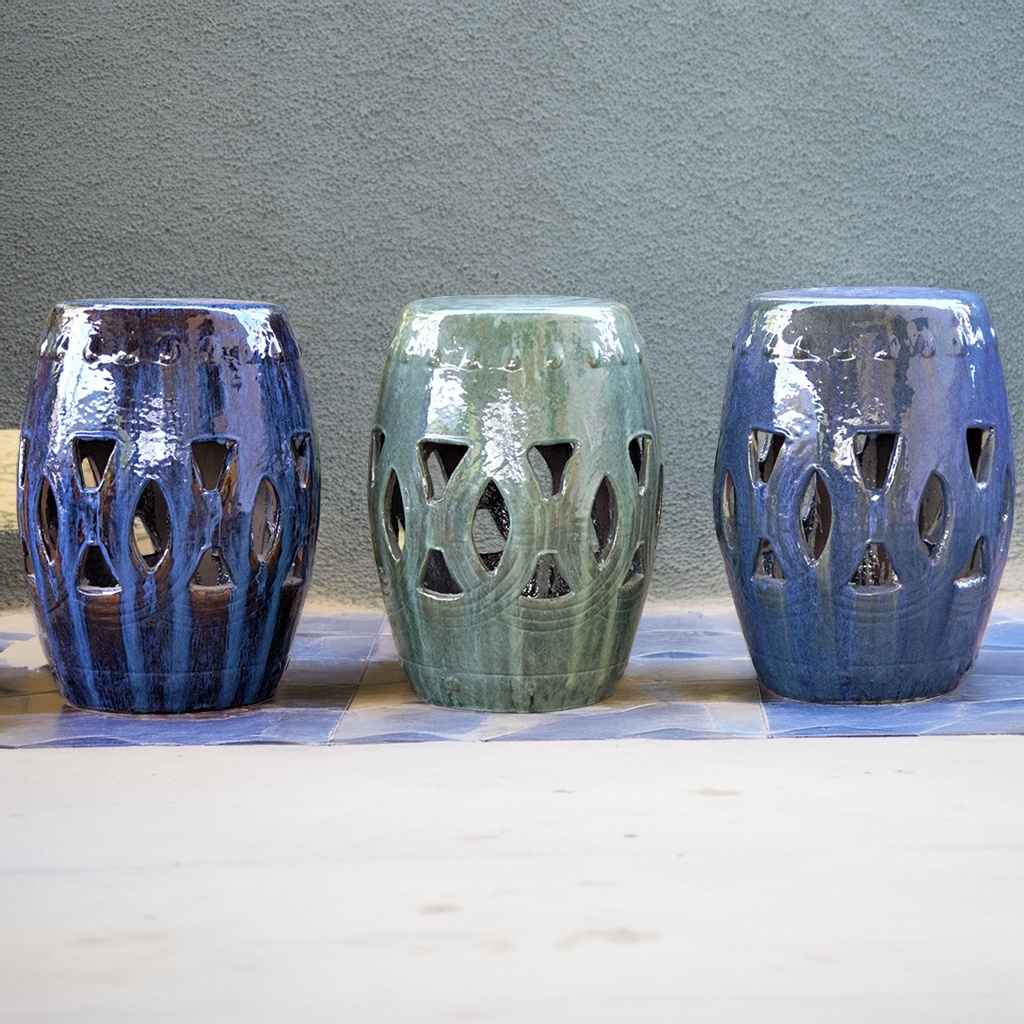 Ceramic garden stools in various glazed hues, including blue and greenish-blue teal, featuring intricate cut-out designs for decorative outdoor seating
