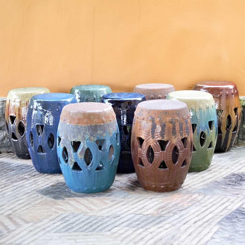 Ceramic garden stools in various hues of blue, green, brown, and cream with decorative cutout patterns for stylish outdoor seating