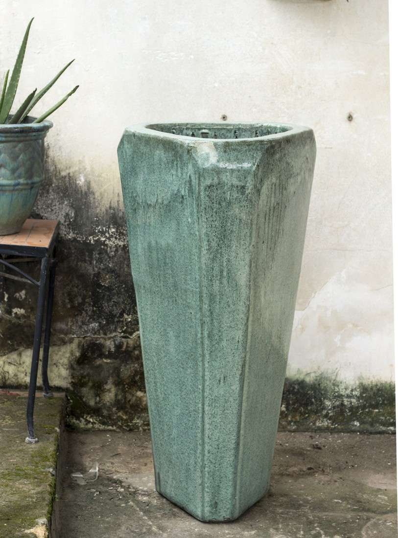 Tall green-glazed ceramic planter with faceted sides, beside a smaller matching pot on a patio.