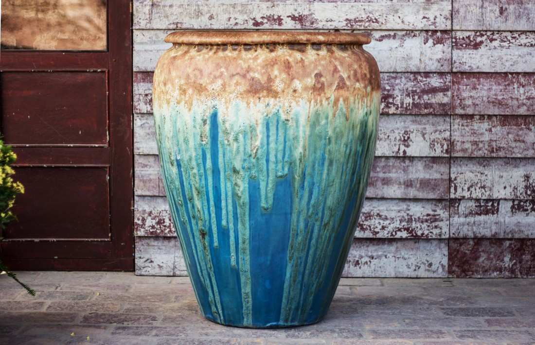 Large ceramic floor vase with drip glaze fading from tan at the rim to deep blue below, beside a wooden door.