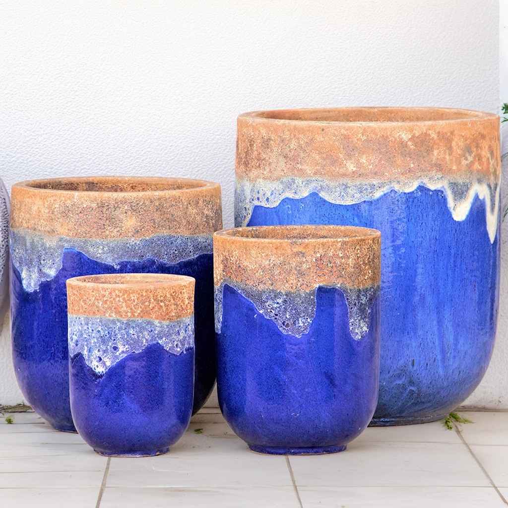 Tall rounded cylinder ceramic planters glazed in blue with a contrasting unglazed rust-colored rim