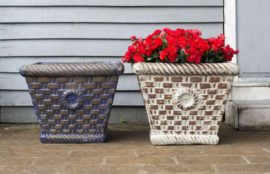 Set of two square ceramic planters with woven basketweave texture, one blue and one white, larger one holding red flowers, on a porch.