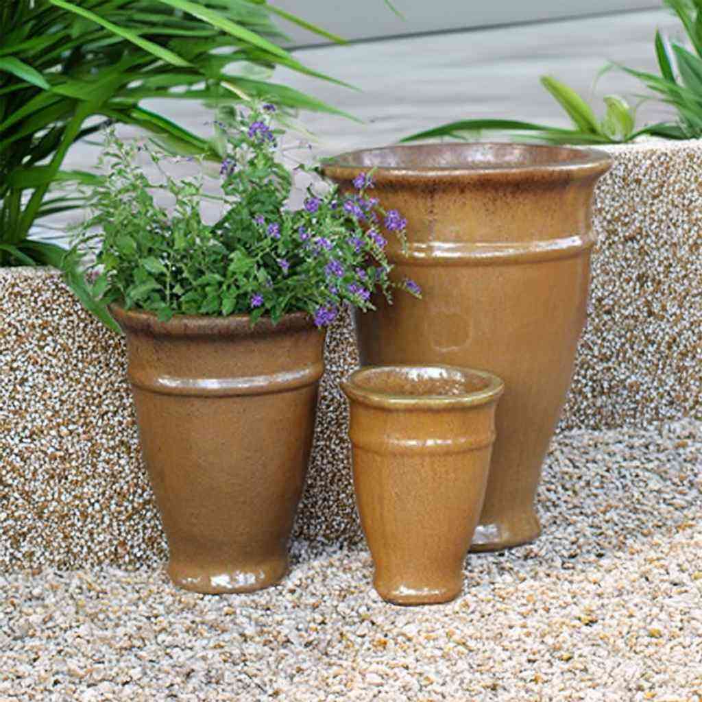 Set of three amber glazed ceramic tapered planters with banded rim, tallest holding purple flowers, on a gravel surface.